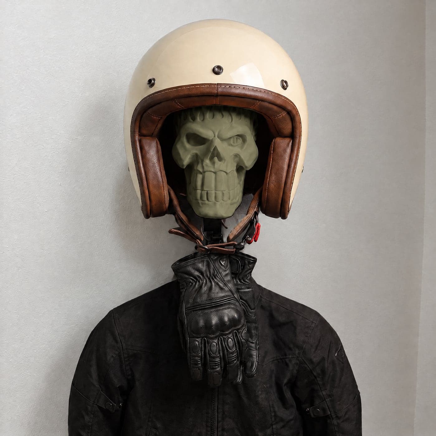 Our mount in Militia Olive wearing a cream open-face helmet with brown leather trim, gloves and a riding jacket hanging below it on a white wall