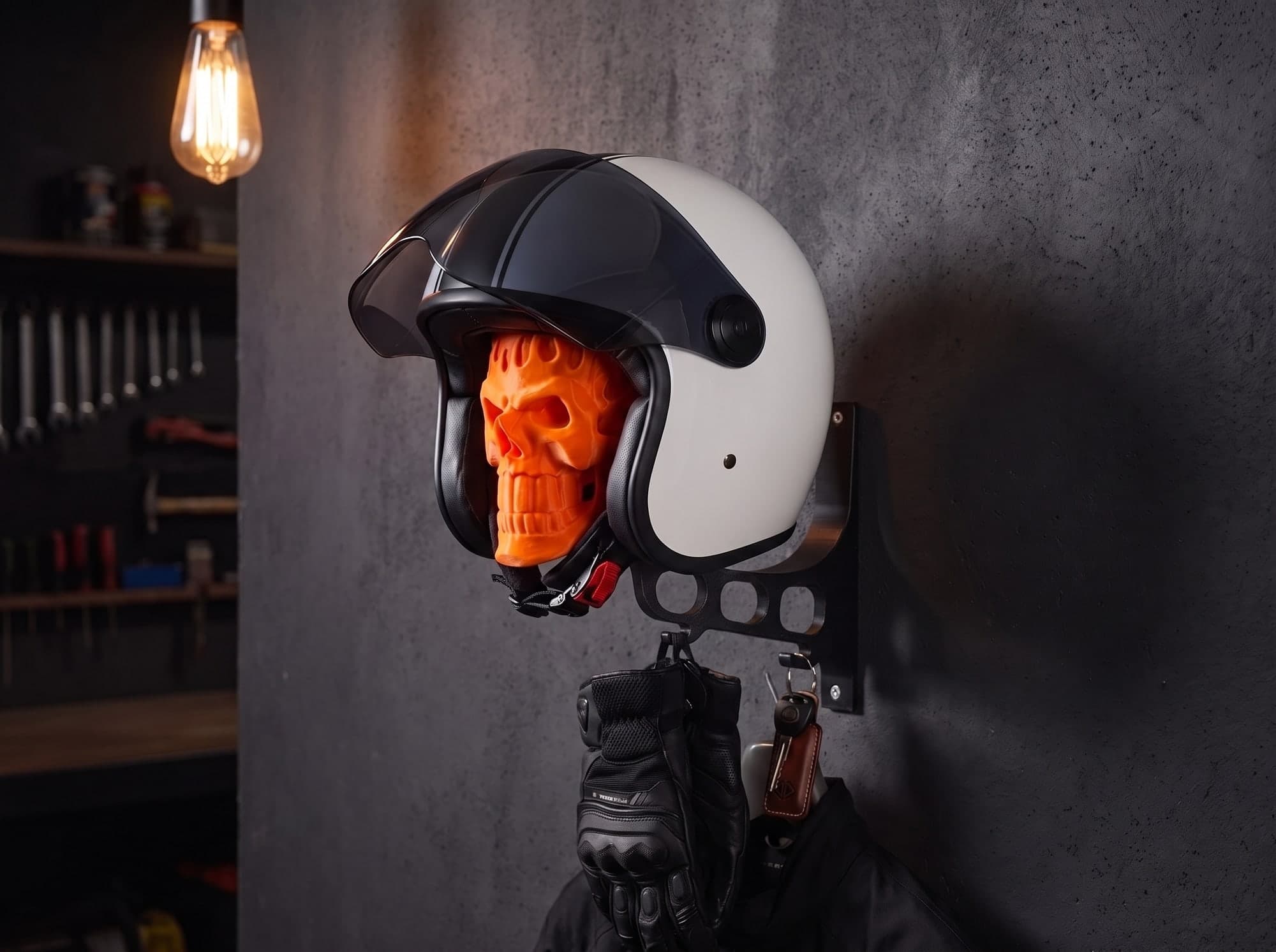 A SKELMET mount on a garage wall at night, a white open-face helmet on the skull and gloves, keys and a jacket on its hooks